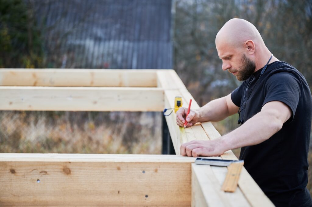 A homeowner marks cuts with a pencil as he completes the frame of his DIY deck construction.